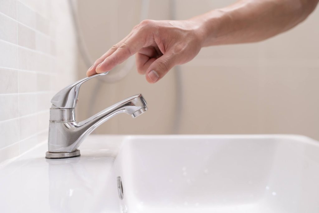 man conserving water by switching off a running water tap