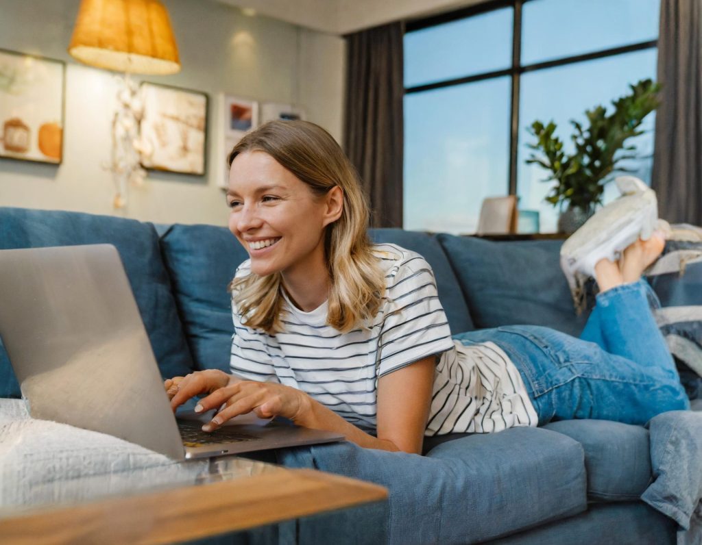 woman laying on sofa while on laptop with tv on