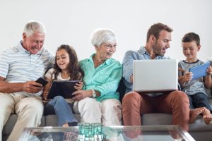 grandparents and grandchildren and son sitting on lounge using devices