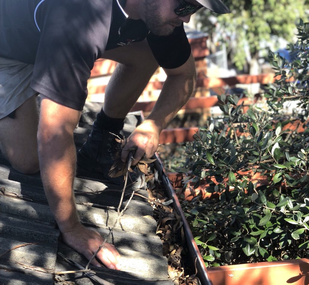 Man clearing debris from a gutter on a roof, a common autumn home maintenance task.