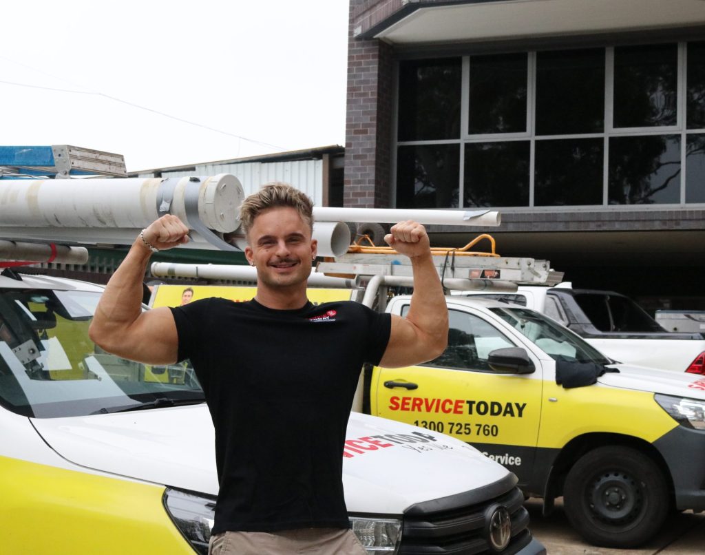 Muscular electrician flexes biceps in front of Service Today vans, offering electrical tips.