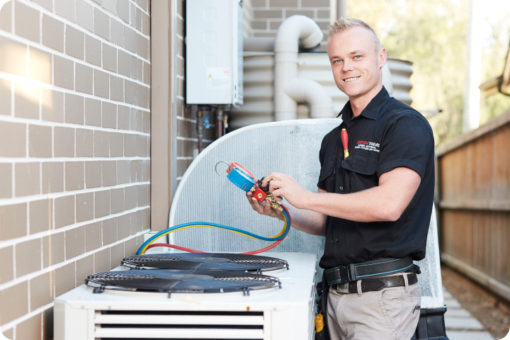 Air conditioning technician with gauges and hoses, servicing outdoor unit.