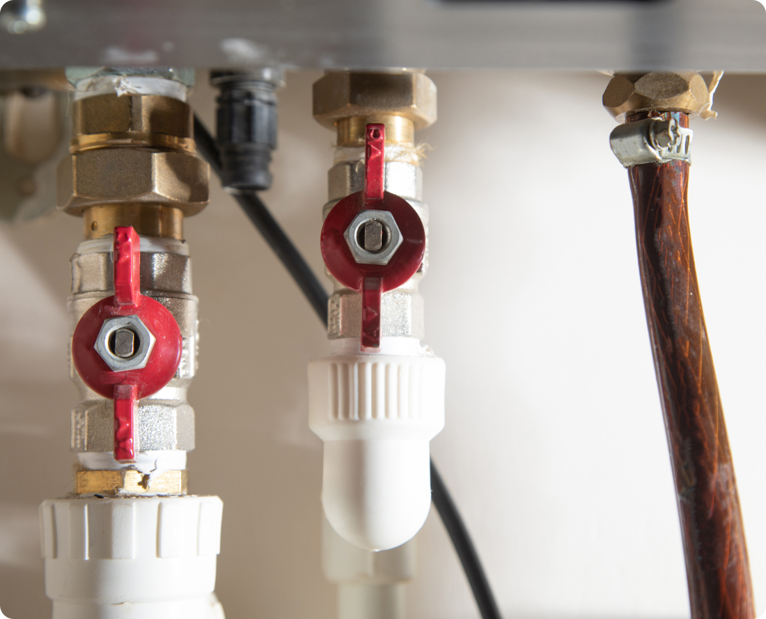 Close-up of plumbing fixtures with red ball valves and a brown hose connected to brass fittings.