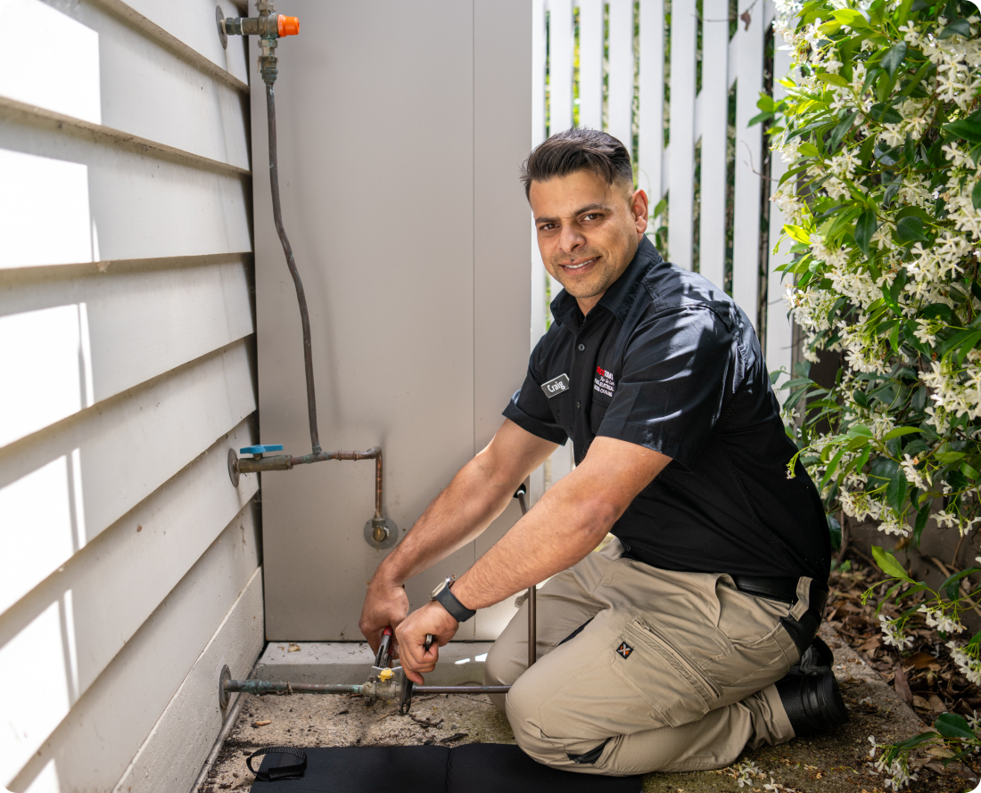 Plumber installing gas pipes, working outdoors next to a building.