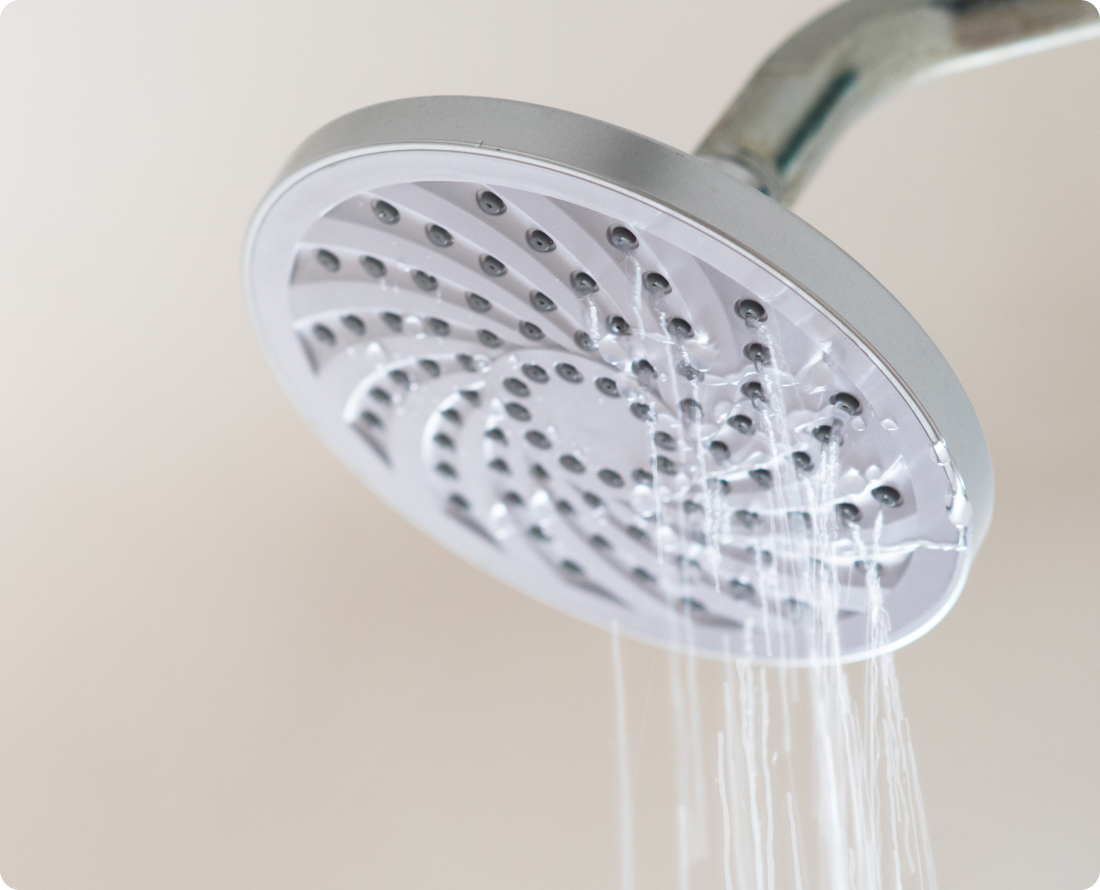 Close-up of a shower head with water spraying from the nozzles, suggesting a leak.