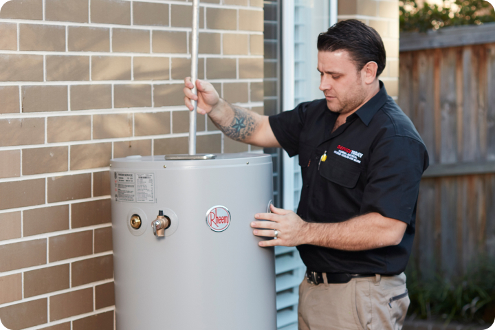 Plumber servicing a Rheem hot water system next to a brick wall.