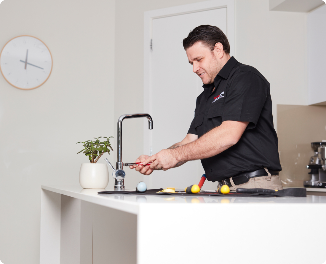 Plumber fixing a kitchen faucet with tools on a countertop.