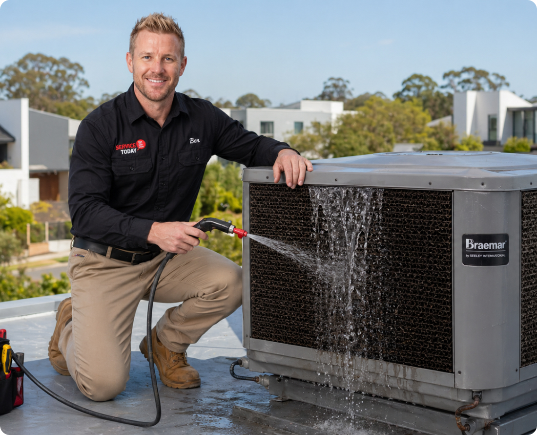 Man cleaning evaporative cooler with hose on a rooftop.