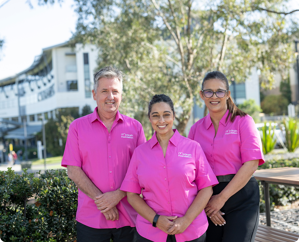 Three McGrath Foundation staff members in pink shirts stand outside a building.