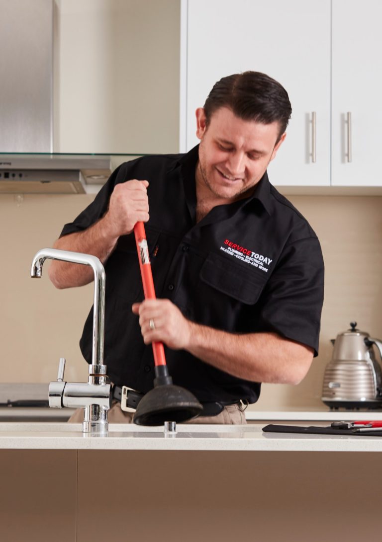 Plumber using a plunger on a kitchen sink, representing plumbing services.