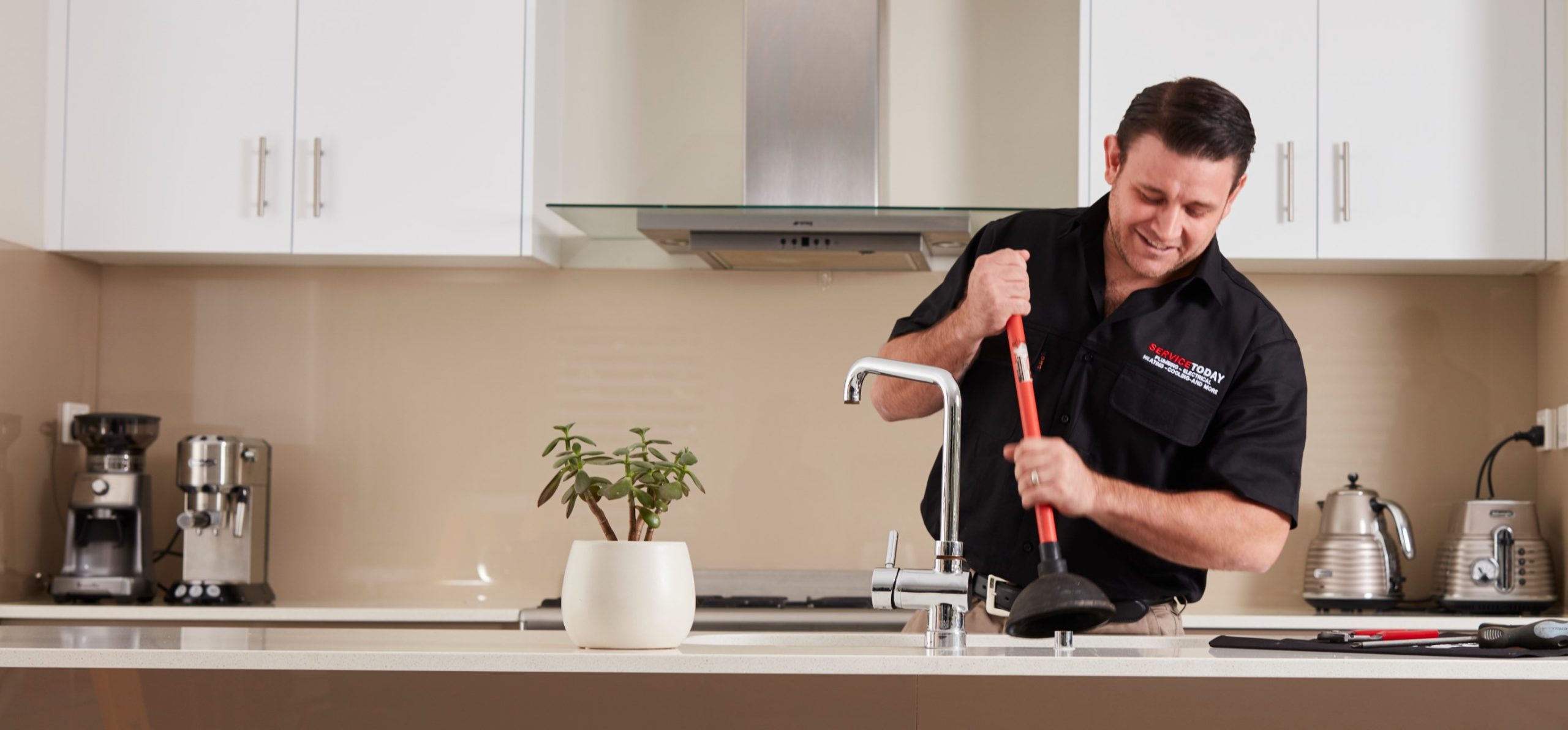 Plumber using a plunger on a kitchen sink faucet.